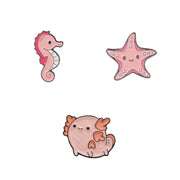 Three cute cartoon sea-themed enamel pins on a plain white background: a pink seahorse, a pink starfish, and a round pink axolotl.