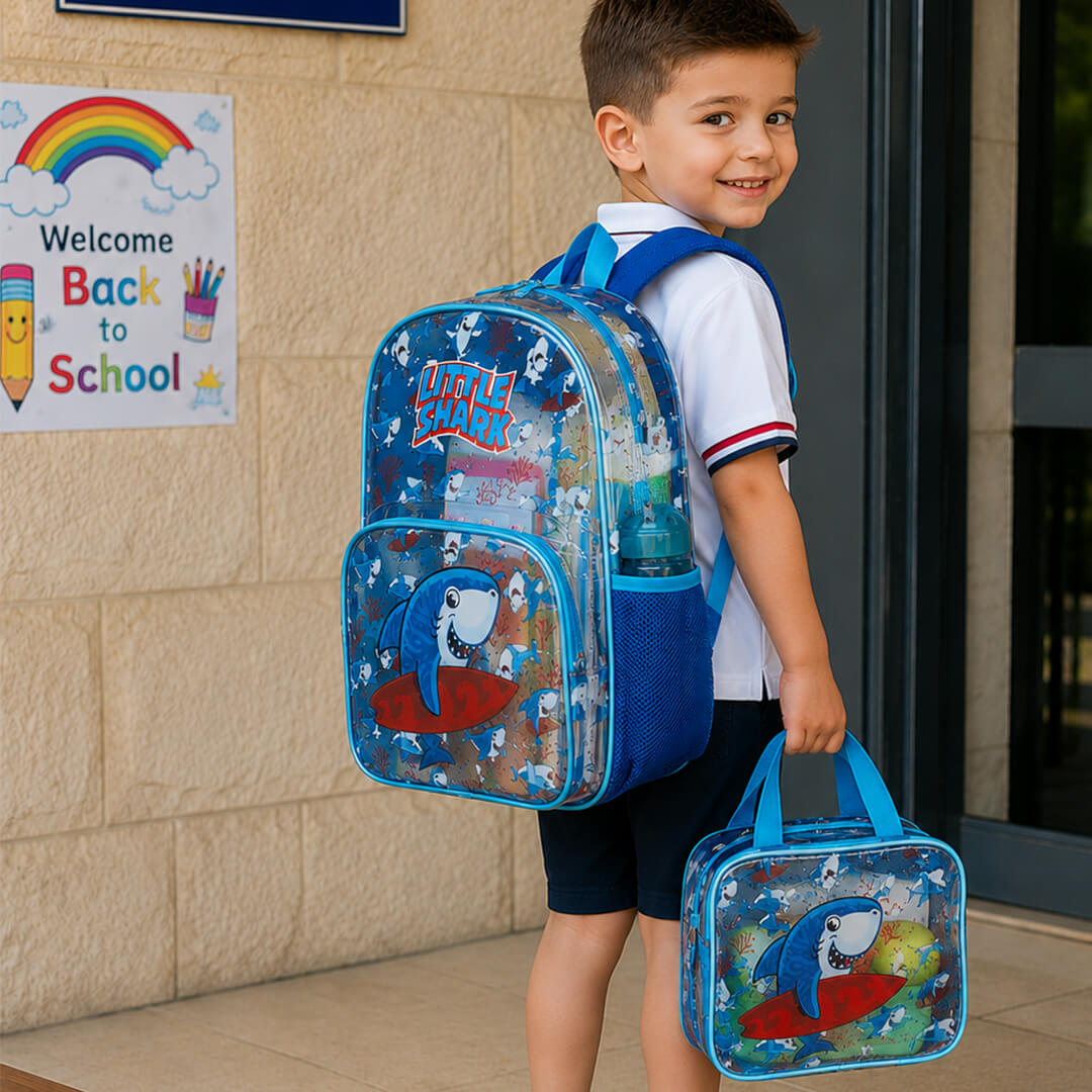 A young boy carrying a blue shark-print school backpack and matching lunch bag.