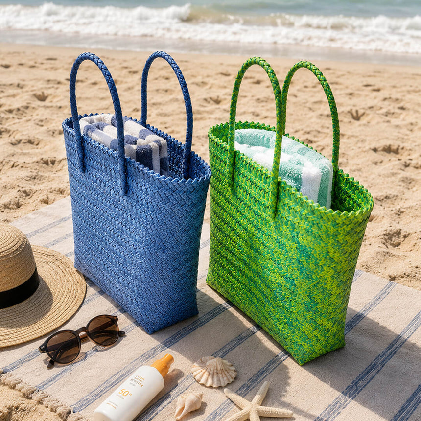 Two woven shoulder bags, one blue and one green, with beach accessories.