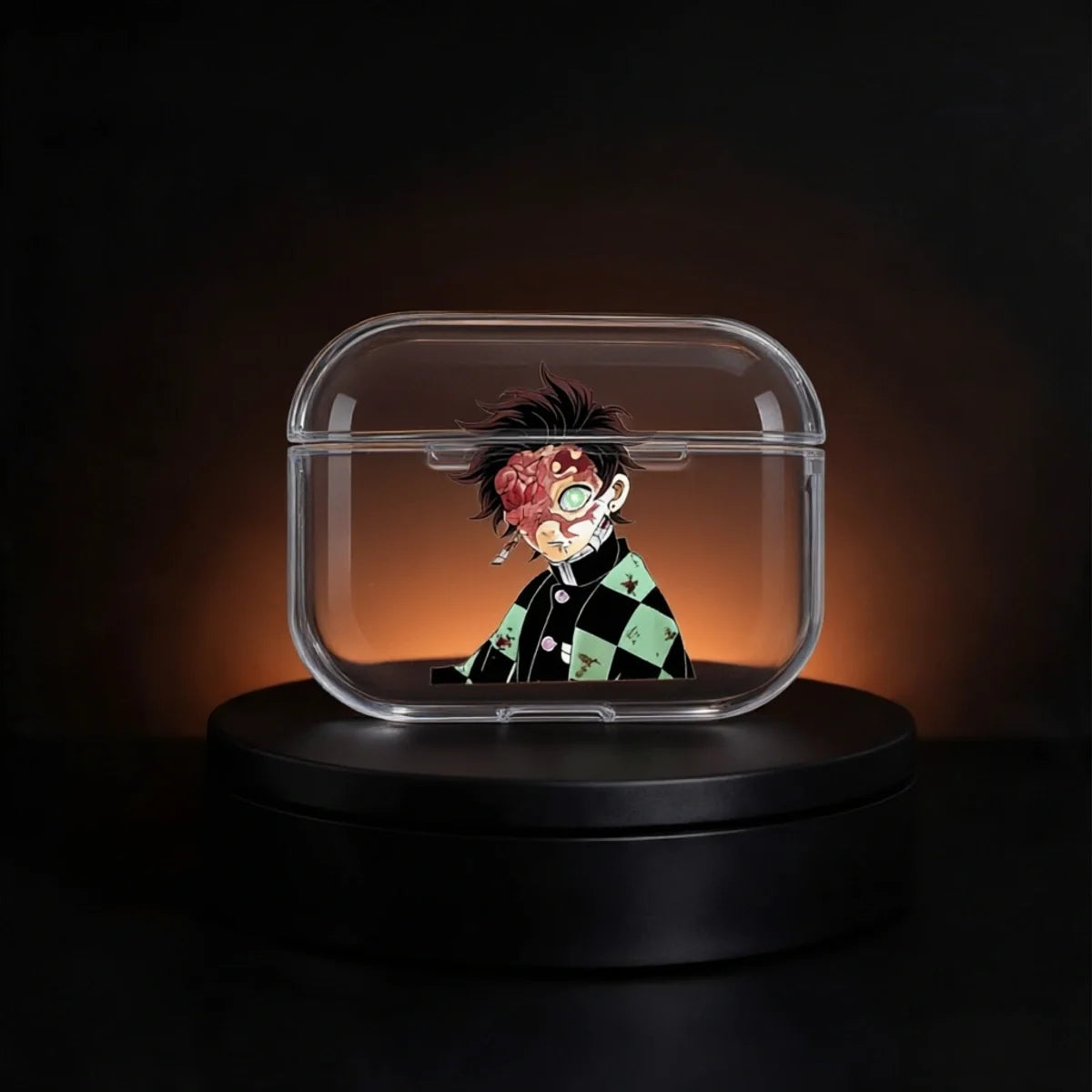 A clear rectangular protective case with rounded corners, shown on a black rotating display base against a dark background with warm orange lighting. The case contains a small anime-style character figure with messy black hair, a red scarred face, and a green-and-black checkered outfit.